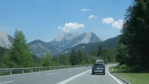 Auto auf einer landschaftlich reizvollen Bergstraße vor einem beeindruckenden alpinen Gebirgspanorama.