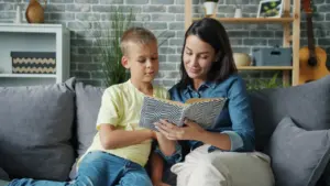 Mutter liest ihrem Sohn zu Hause auf einem Sofa ein Buch vor.