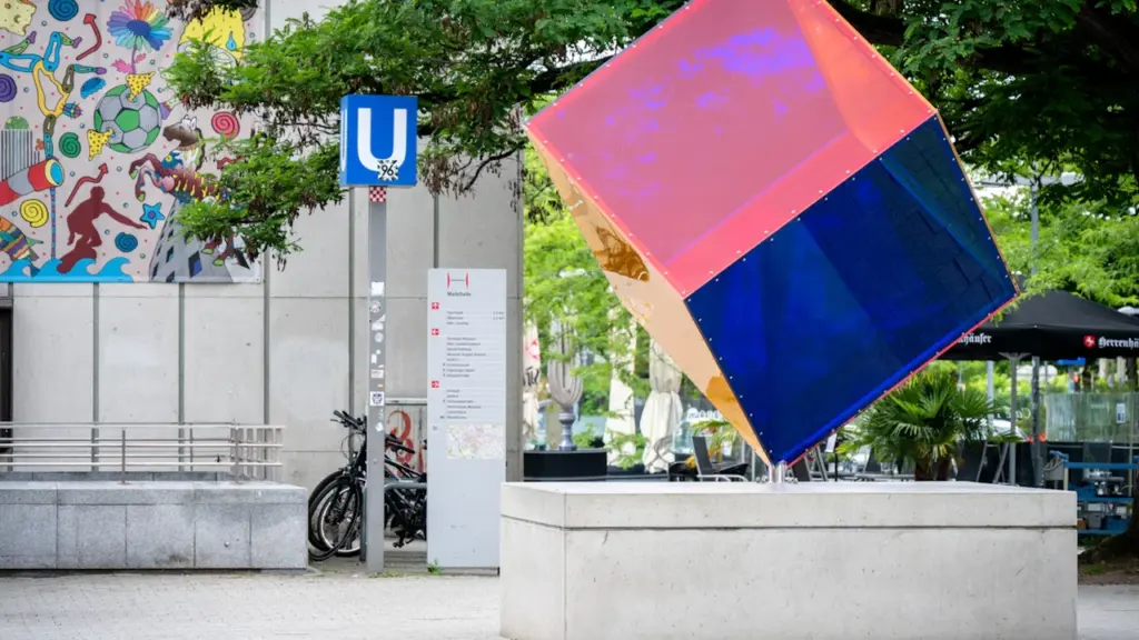 Bunte, schillernde Würfel-Skulptur in einem städtischen Umfeld im öffentlichen Raum.