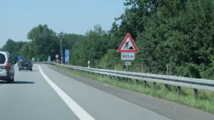 Ein gelbes Baustellenschild am Straßenrand signalisiert den Beginn der Bauarbeiten auf der Autobahn.