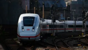 Moderner weißer ICE-Zug fährt auf Gleisen durch ein deutsches Stadtgebiet.