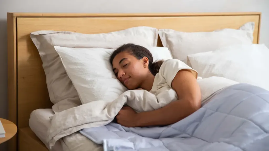 Eine entspannt schlafende junge Frau in einem hellen, aufgeräumten Schlafzimmer mit weißen Laken.