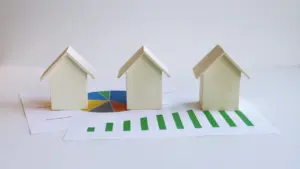 Drei kleine Modellhäuser auf einer Grafik mit steigendem grünem Balkendiagramm und Tortendiagramm.