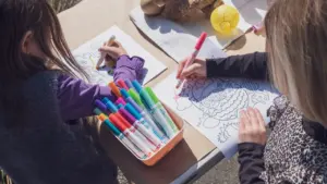 Zwei Kinder malen konzentriert mit bunten Stiften an einem Tisch beim Basteln