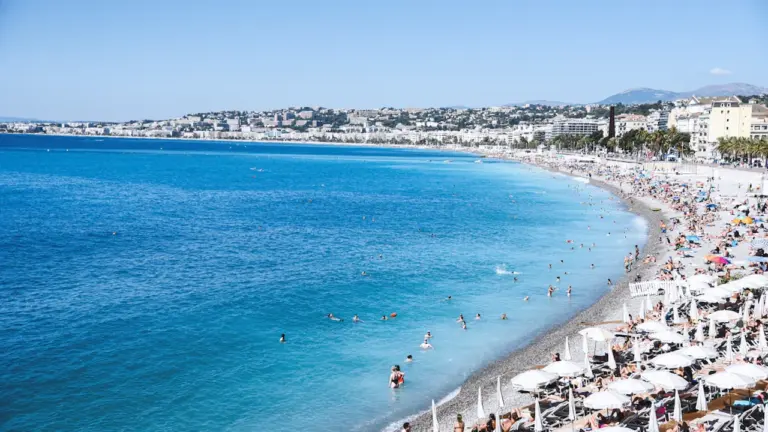 Überfüllter Strand mit blauem Meer und zahlreichen weißen Sonnenschirmen in Südeuropa