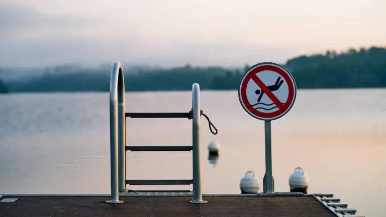 Verbotsschild für das Baden an einem hölzernen Steg bei einem ruhigen See.