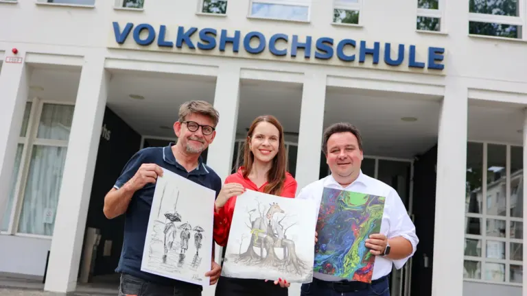 Drei Personen halten vor einer Volkshochschule jeweils ein eigenes Kunstwerk in die Kamera.