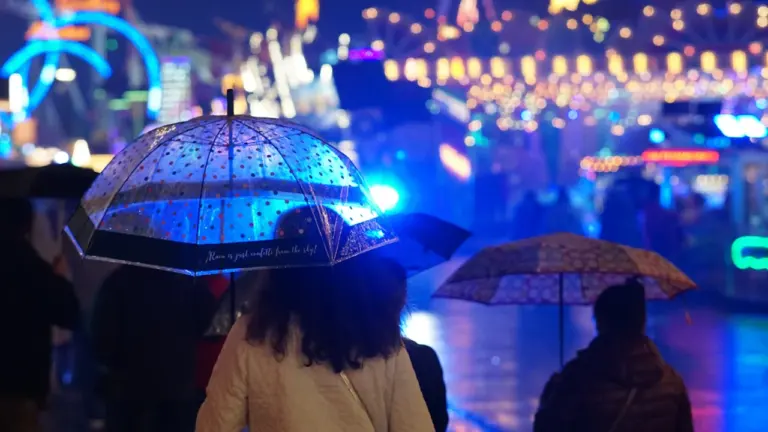 Besucher nutzen bei Regen Schirme auf dem nächtlichen Oktoberfest in München.