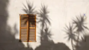 Geschlossene Fensterläden an einer hellen Hauswand spenden an heißen Sommertagen kühlen Schatten.