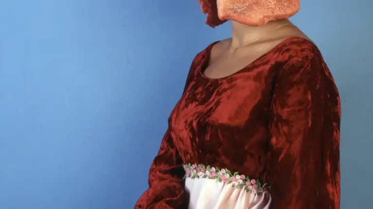 Eine Frau in einem viktorianischen Samtkleid trägt ein rohes Fleischstück als Kopfbedeckung.