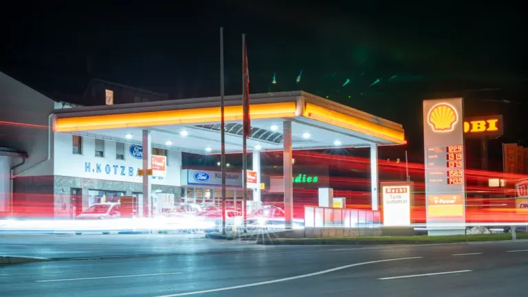 Eine nächtliche Tankstelle in Deutschland mit beleuchteter Preisanzeige und vorbeifahrenden Autos.
