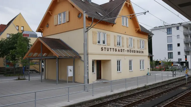 Historisches Bahnhofsgebäude in Stuttgart-Möhringen mit moderner Straßenbahnlinie und gelber Holzfassade.