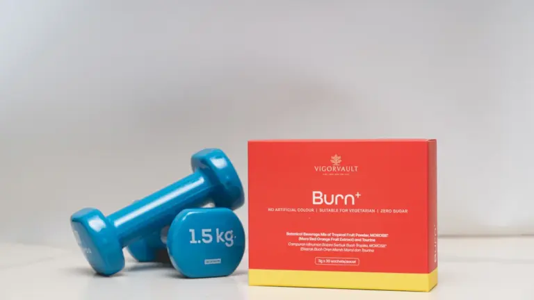Blaue Hanteln und eine rote Supplement-Packung vor einem schlichten, neutralen Hintergrund.
