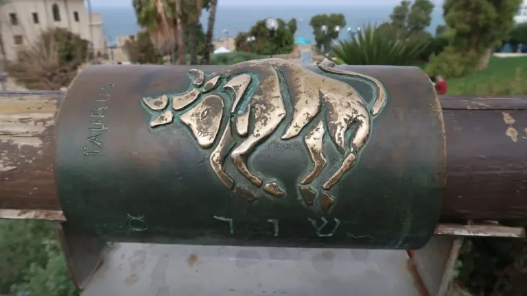 Bronzefarbene Reliefdarstellung eines Stiers auf einem zylindrischen Denkmal im Freien.