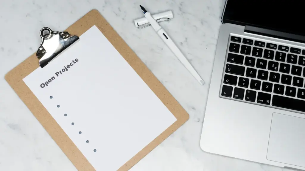 Ein Klemmbrett mit der Aufschrift offene Projekte neben einem modernen silbernen Laptop.