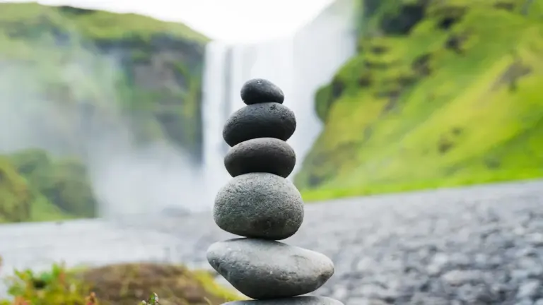 Ein Steinturm vor einem Wasserfall symbolisiert Ruhe und natürliche Balance.