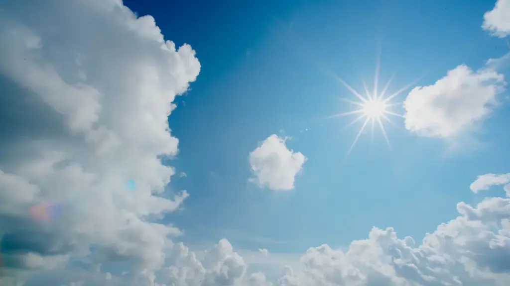 Heller blauer Himmel mit strahlender Sonne und weißen Wolken an einem heißen Sommertag.