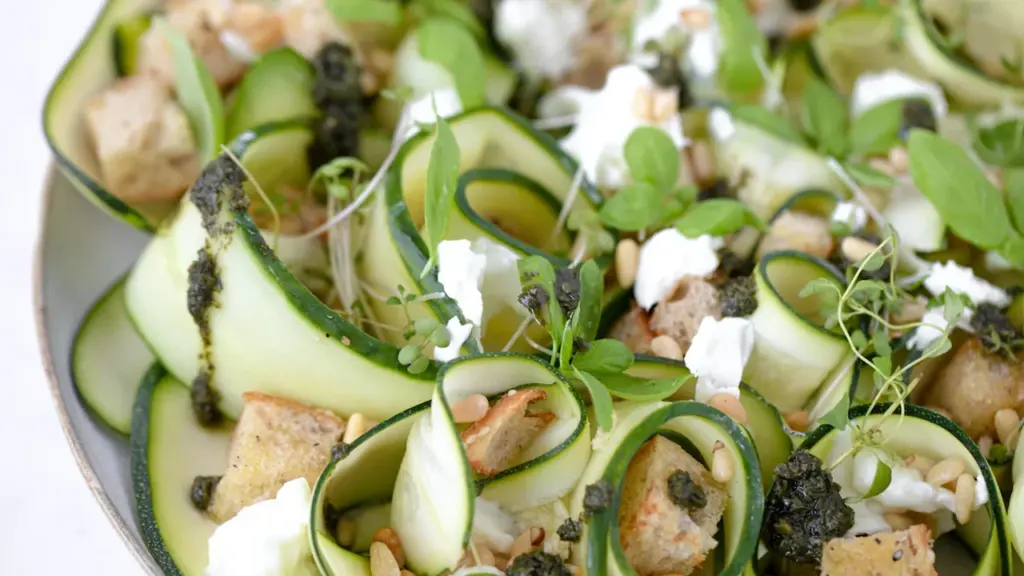 Nahaufnahme einer frischen Zucchini-Pfanne mit Feta, Kräutern und Kirschtomaten auf einem Teller.