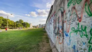 Die Berliner Mauer mit Graffiti vor einer grünen Parklandschaft und Stadtansicht.