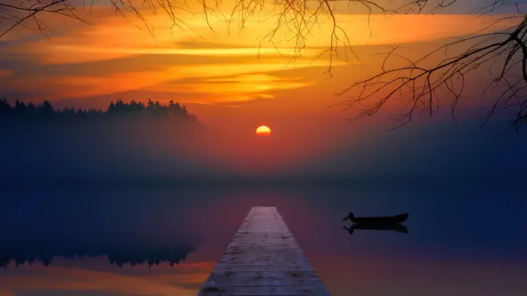 Ein hölzerner Steg führt in einen nebligen, ruhigen See bei Sonnenaufgang in Bayern.