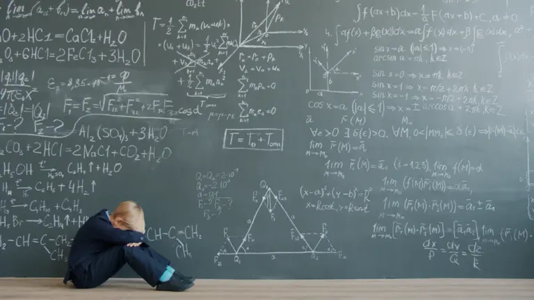 Ein erschöpftes Kind sitzt vor einer mit mathematischen Formeln beschriebenen Tafel auf dem Boden.