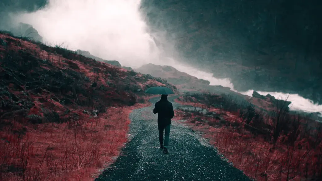 Eine einsame Person mit Regenschirm geht einen nebligen Pfad durch eine karge, bergige Landschaft entlang.