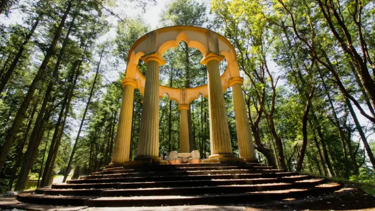 Ein einsamer, antiker Pavillon in einem ruhigen, grünen Wald bei Tageslicht.